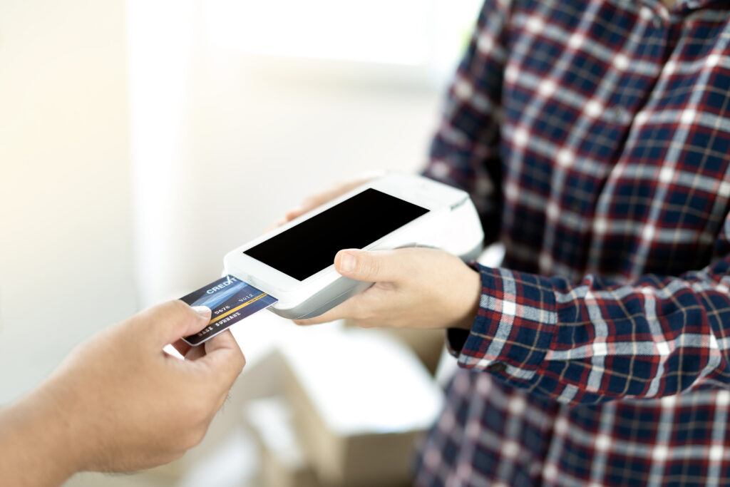 Close-up of asian entrepreneur using EDC to receive credit card for payment from customer in her store.